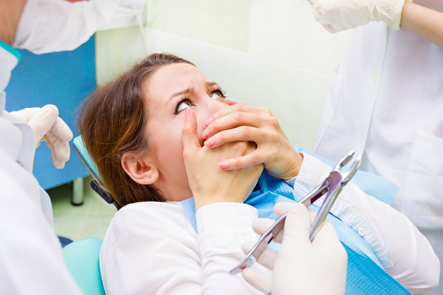 Paura del dentista: paziente donna spaventata si copre la bocca