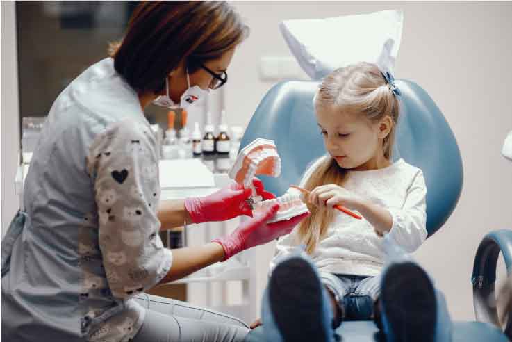 paura del dentista: bambina che si approccia a conoscere i denti con l'assistente alla poltrona